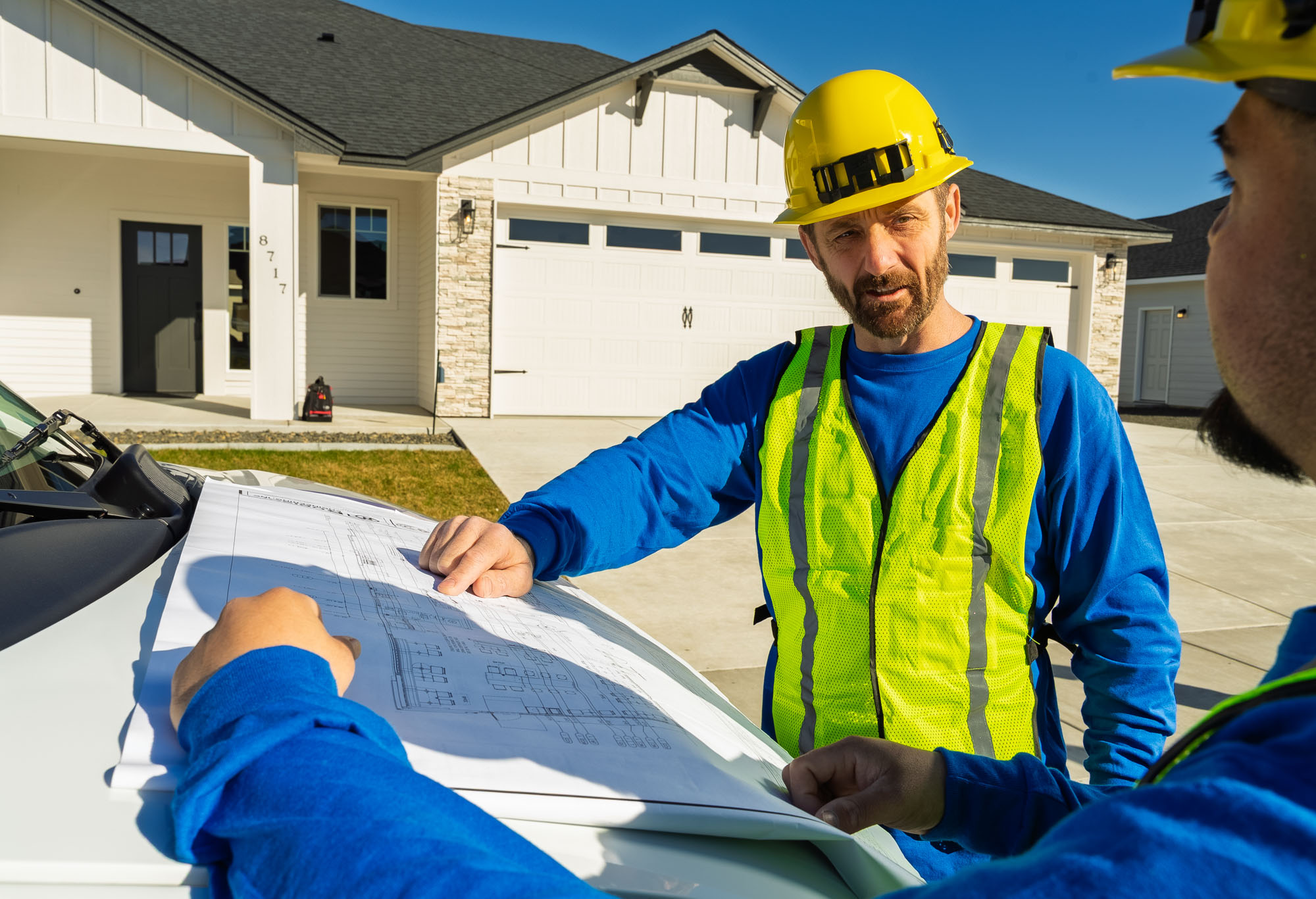 Construction workers reviewing blueprints outside house.