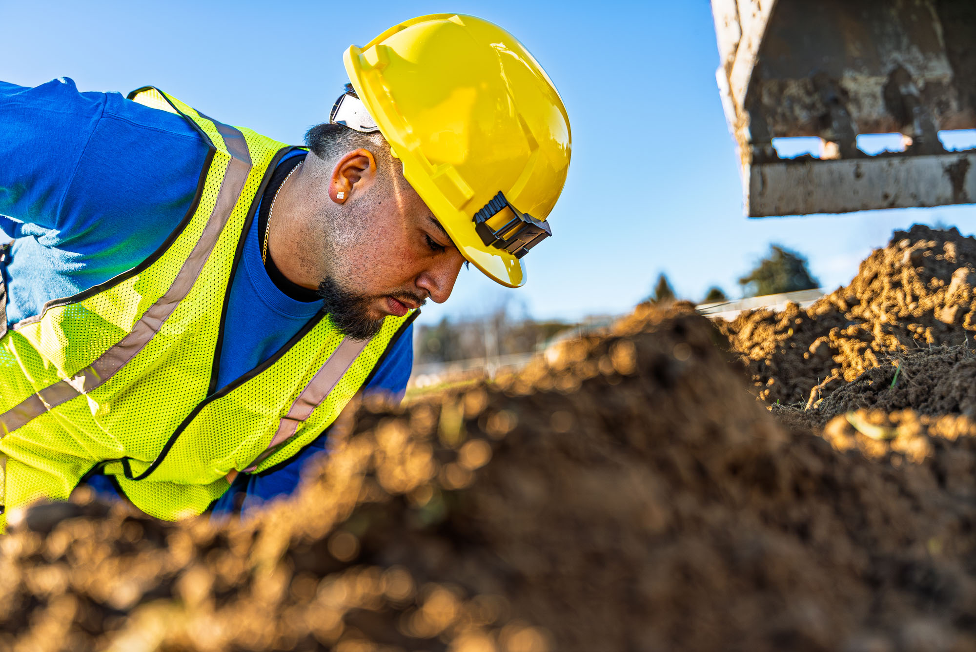 Construction worker inspecting dug soil on-site.