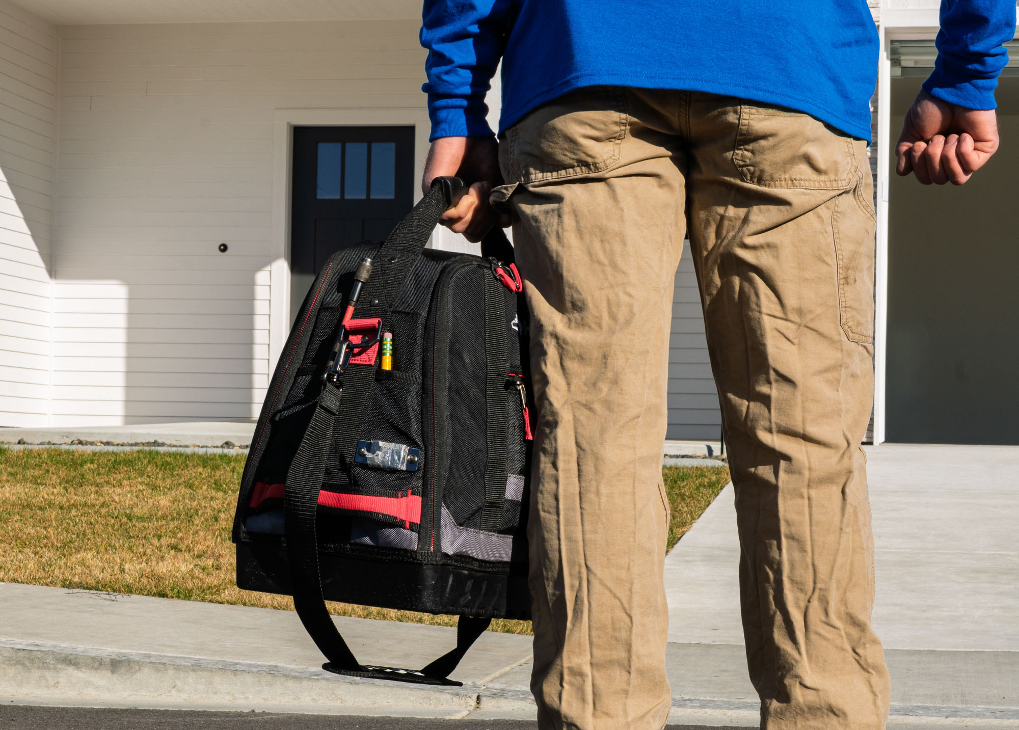 Person holding tool bag outside home.