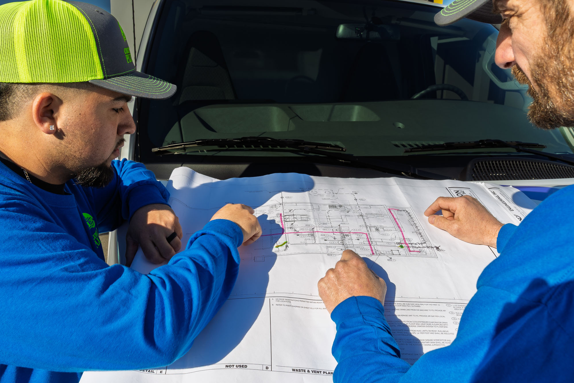 Two men discussing construction plans on vehicle hood.